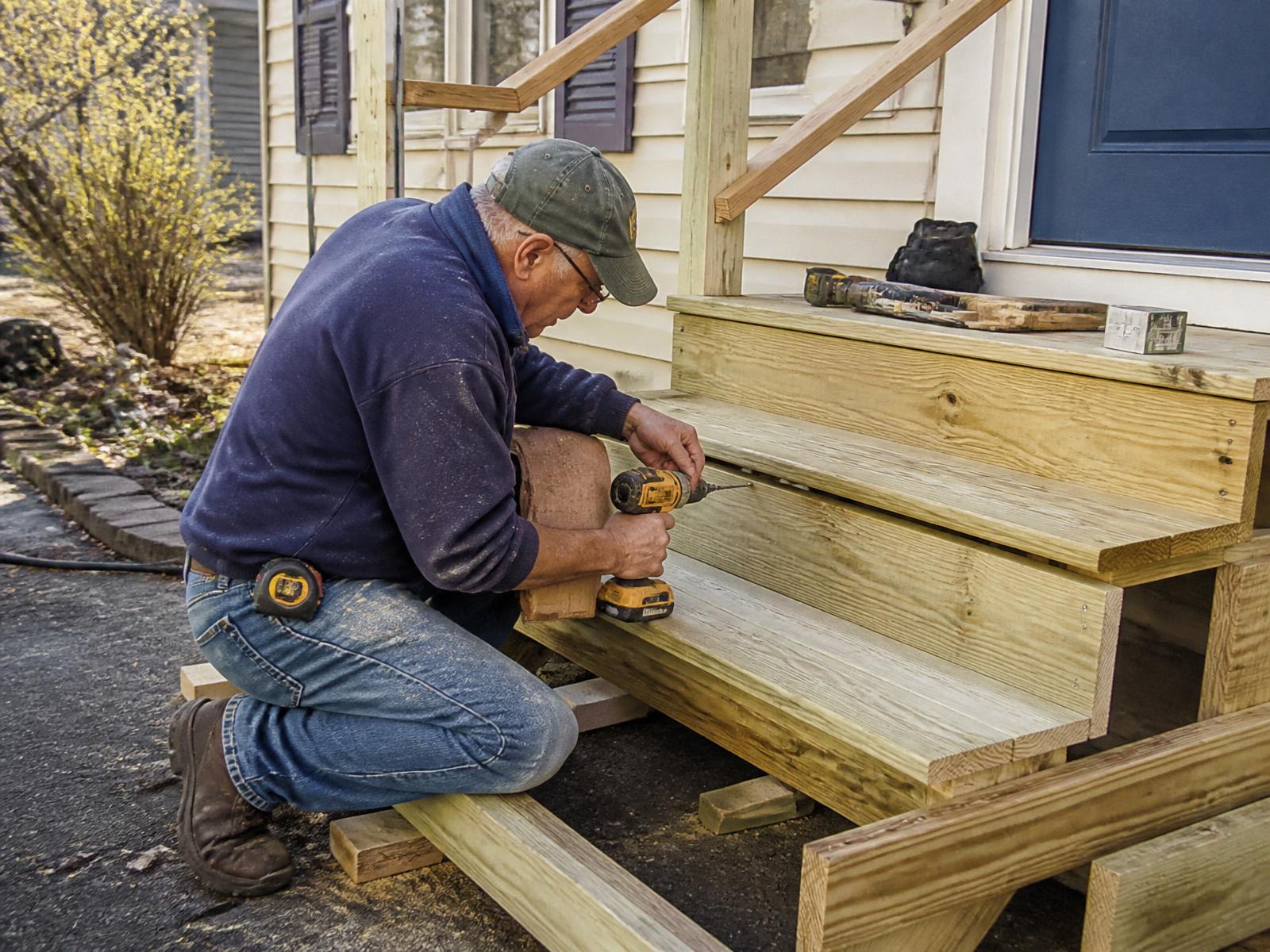 Carpenter rebuilding wooden porch steps with fresh lumber